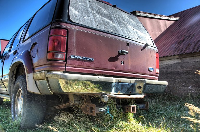 A rusted, dirty Ford Explorer SUV is parked in a field with a corrugated metal building behind it.