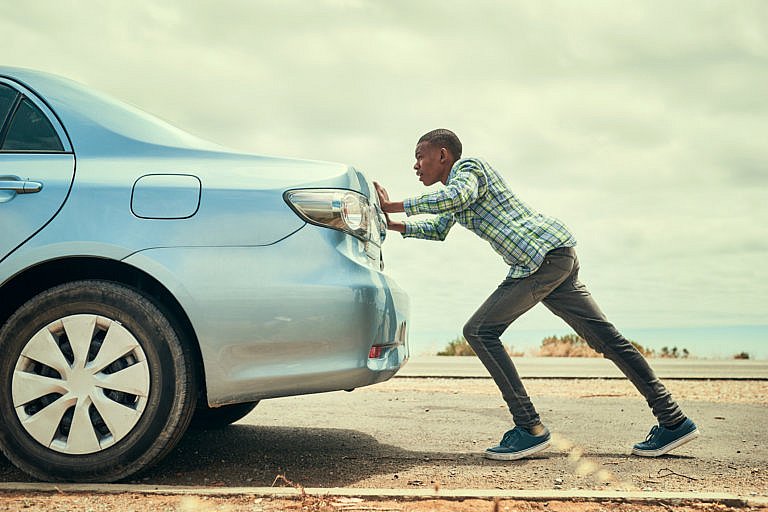 A man is pushing a blue car on the side of the road.