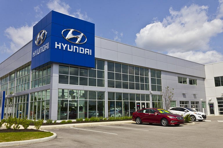 A red and a white car parked in front of a Hyundai dealership.
