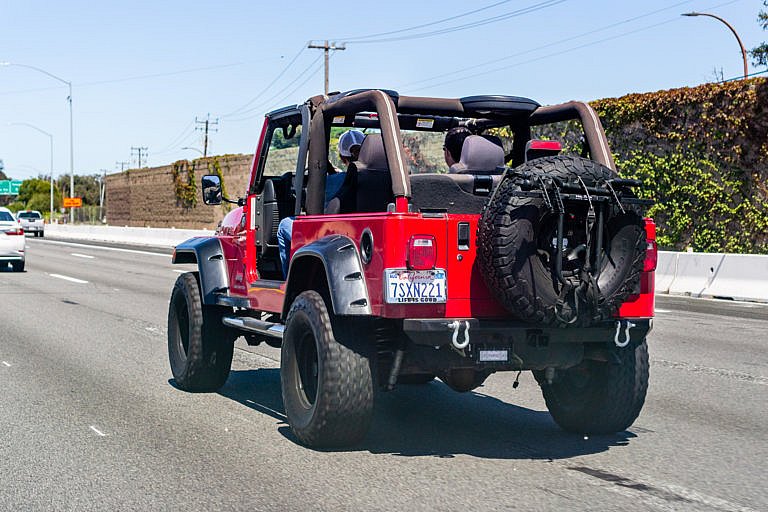 Red Jeep Wrangler driving on the highway with the top down.