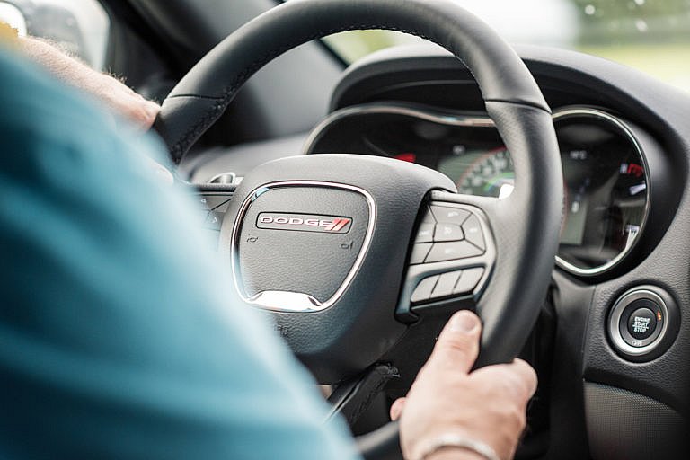A driver's hands are on the steering wheel of a Dodge vehicle, with a 
