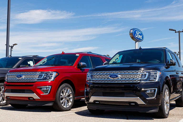 A red and a black Ford SUV are parked near a Ford sign.