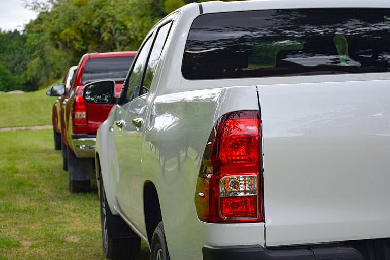A close-up of two pickup trucks, one white and one red, parked on grass.