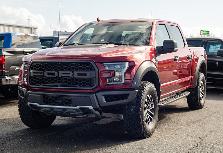 A red Ford Raptor pickup truck is parked in a lot.