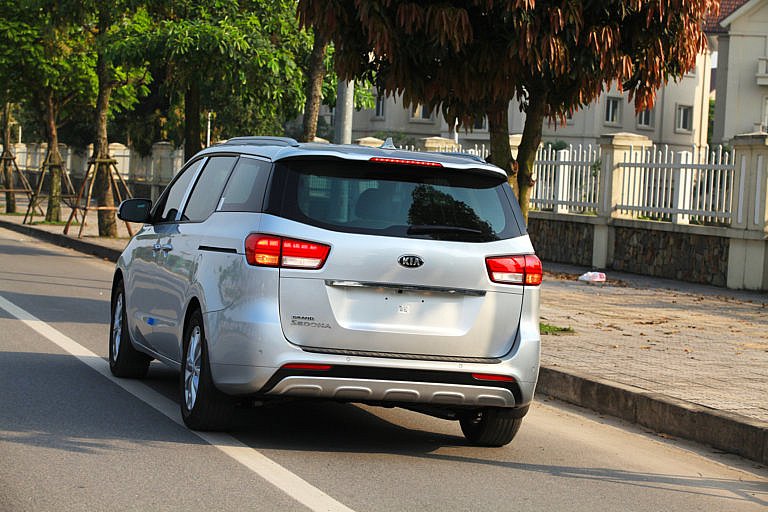 A silver Kia Grand Sedona minivan is parked on a street.