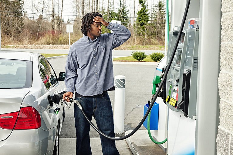 Man refueling car at gas station looking frustrated.