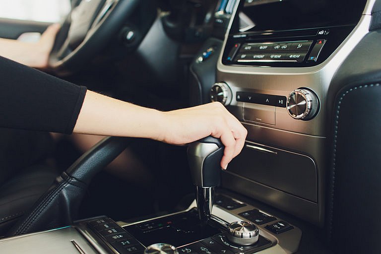 Hand holding a car’s gear shift lever inside the vehicle.
