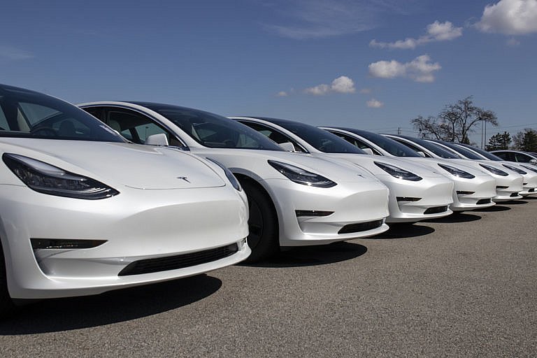 A row of white Tesla Model 3 cars are parked together.
