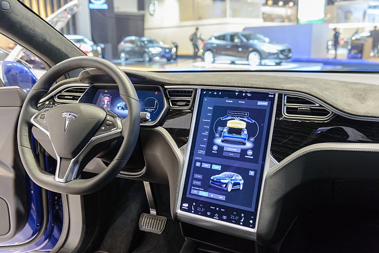 A Tesla steering wheel is shown with a touchscreen display.
