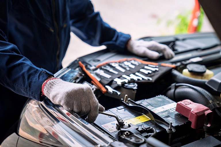 A mechanic wearing work gloves is using a wrench to work on a car's engine. A set of tools is visible in the background.