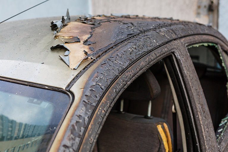 A severely damaged car is shown with its roof and door frame charred and peeling. The interior is also visible, showing signs of fire damage.