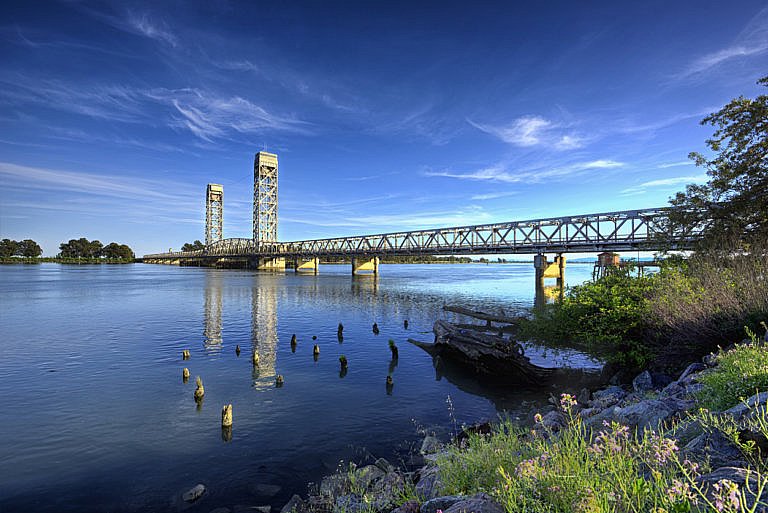 Steel drawbridge spanning a calm river under a clear blue sky