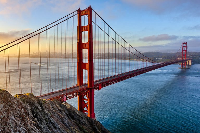 The Golden Gate Bridge spans across the bay at sunset with the city in the distance.