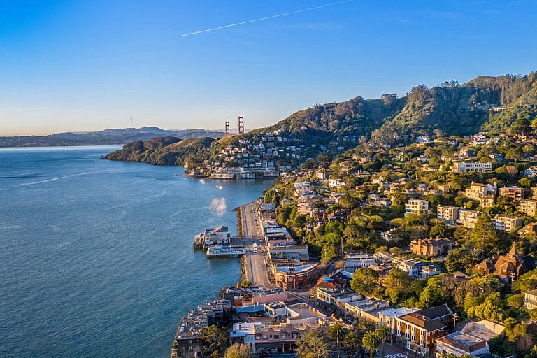 A coastal hillside town overlooks the bay with the Golden Gate Bridge in the distance.