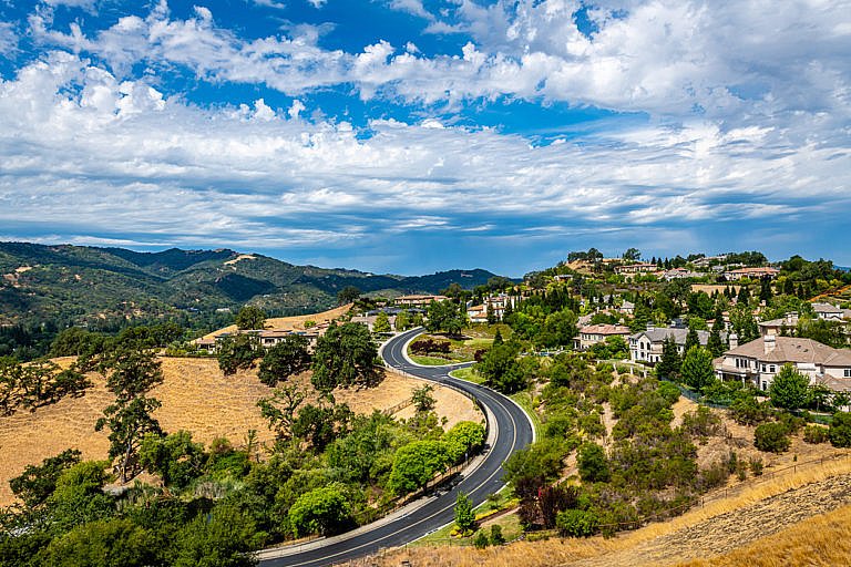 A winding road curves through a hillside neighborhood with mountains in the background.