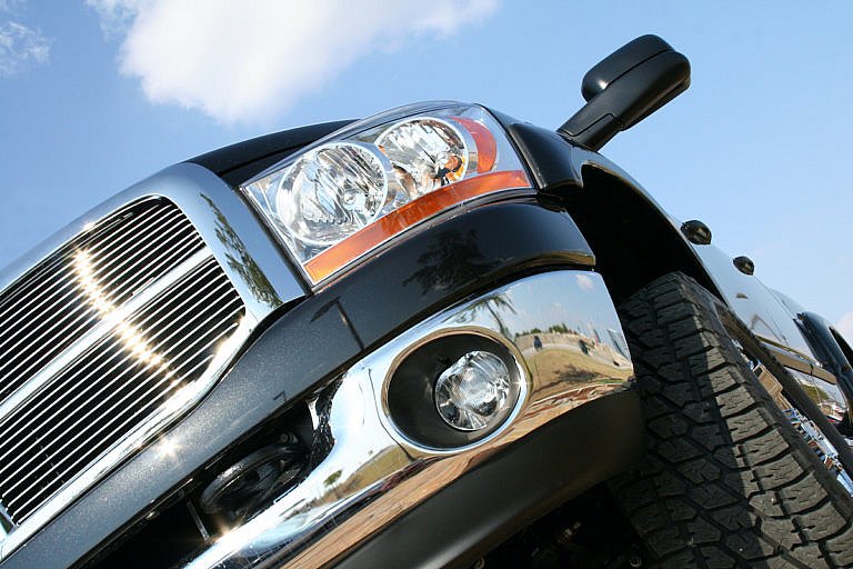 A low-angle shot of the front of a black pickup truck, featuring a chrome grille and bumper, with a bright blue sky in the background.