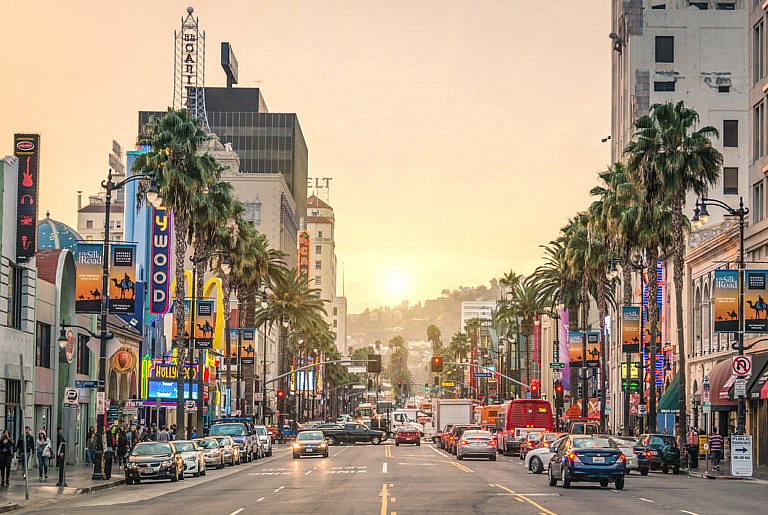 Busy Hollywood Boulevard with cars, palm trees, and neon signs at sunset
