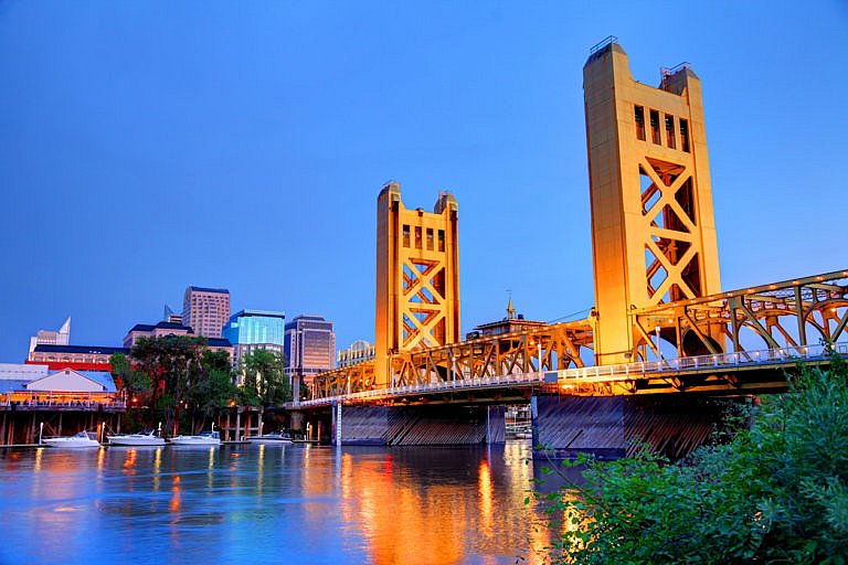 Tower Bridge in Sacramento illuminated at dusk with city skyline in background.