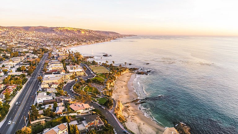 A coastal cityscape at sunset with sandy beaches, ocean waves, and hillside homes.