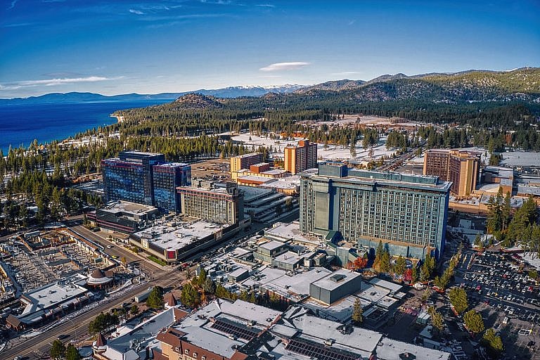 Aerial view of a city with tall hotels near a lake and forested mountains.