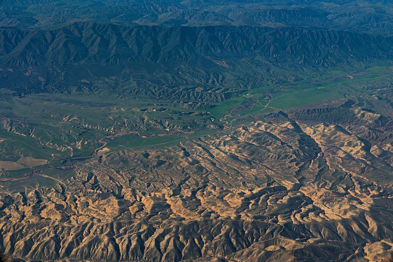 Aerial view of rugged mountains with winding valleys and green farmland