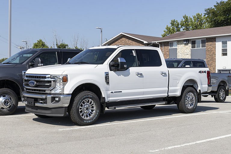 A white Ford Super Duty pickup is parked at a dealership.
