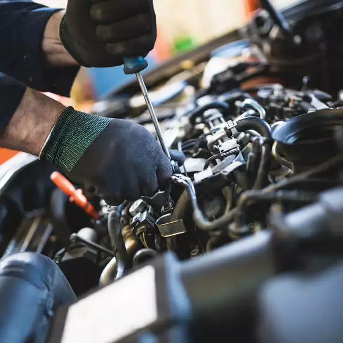 Mechanic using a screwdriver to repair a car engine with gloves on.