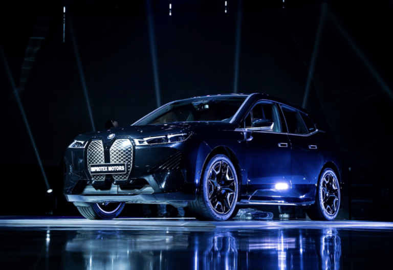 A sleek, dark BMW iX electric SUV is on display under a dramatic blue light.