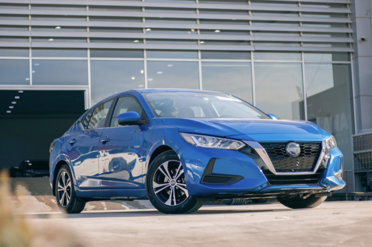 A modern, bright blue Nissan sedan parked in front of a glass building.