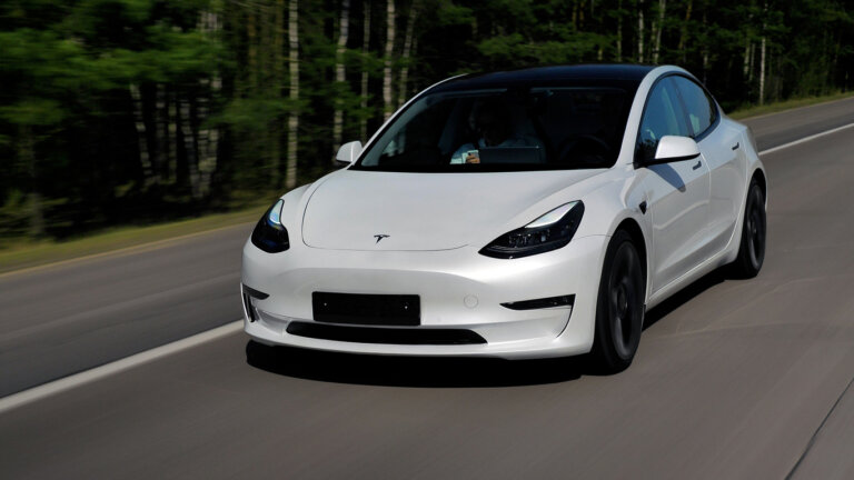 A white Tesla Model 3 is driving on the road.