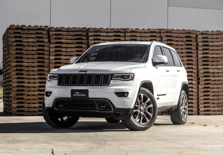 White Jeep Grand Cherokee parked near stacked wooden pallets.