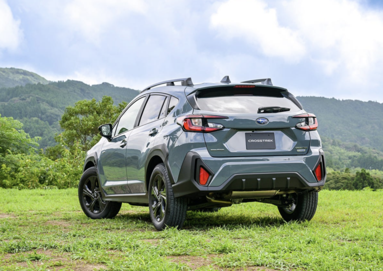 A Subaru Crosstrek SUV parked on grass with mountains in the background.