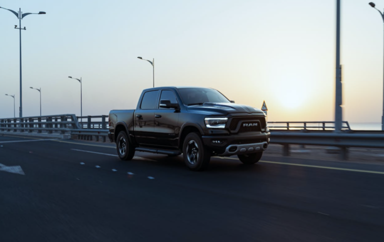 A black Ram pickup truck driving on a coastal highway at sunset.