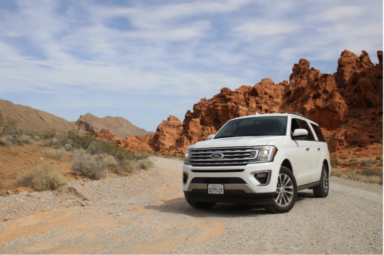 A white Ford SUV drives near red rock formations.
