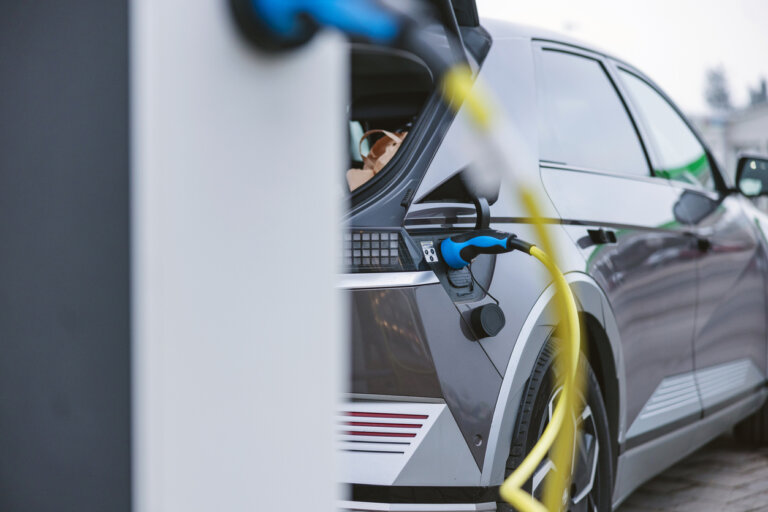 A car is plugged into an electric vehicle charging station, with a yellow charging cable connecting the vehicle to the station.
