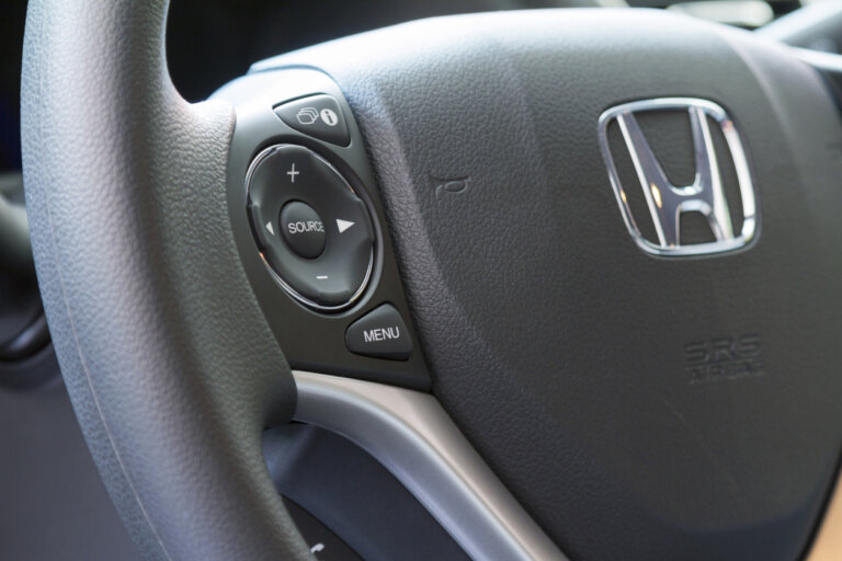 A detailed shot of a Honda steering wheel, showcasing its controls and the chrome emblem.