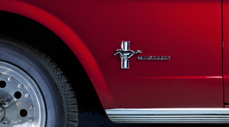 A red classic Ford Mustang shows its side emblem.