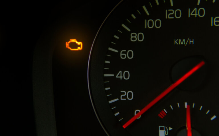 A car dashboard with an illuminated check engine light and speedometer in km/h.