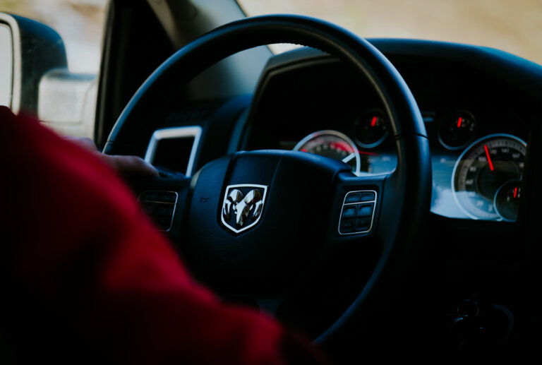 Driver holding the steering wheel of a Dodge vehicle with gauges visible in the dashboard