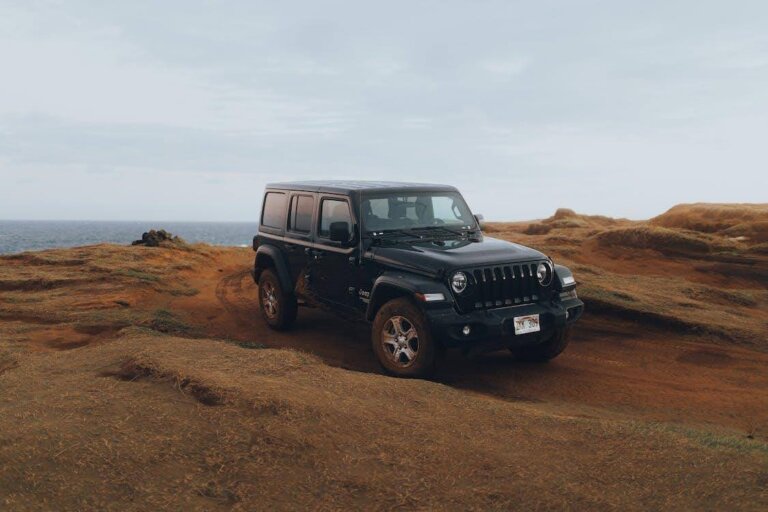 Black Jeep SUV driving on rocky terrain near the ocean.