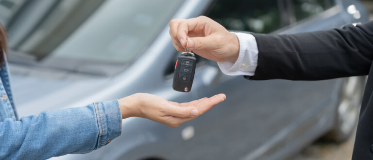A hand in a suit jacket is handing a car key fob to a person wearing a denim jacket.