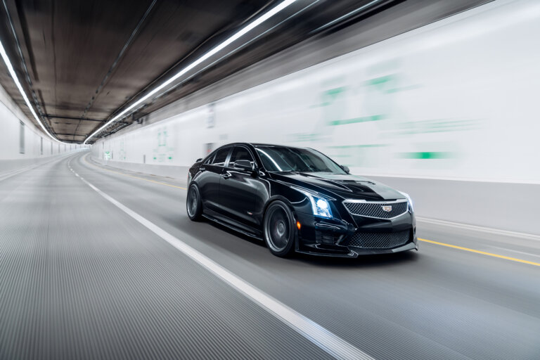 A sleek black Cadillac drives through a modern tunnel at high speed.