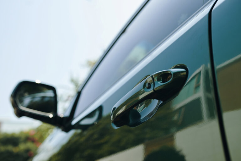 Alt-text suggestion: **Close-up of a black car door handle and side mirror in daylight**