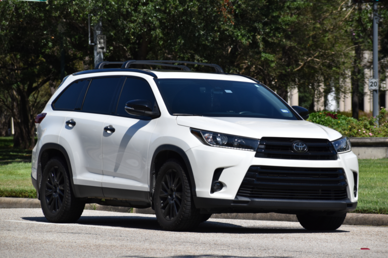 White Toyota SUV parked on a street near trees