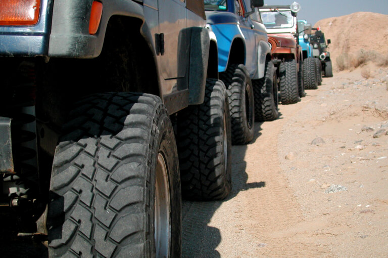 Line of off-road Jeeps with large tires driving on sandy terrain.