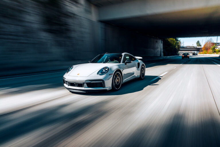 White Porsche sports car driving fast on the highway under an overpass.