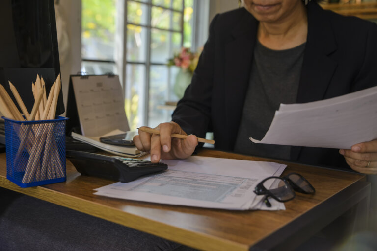 A person is reviewing documents and using a calculator at a desk.