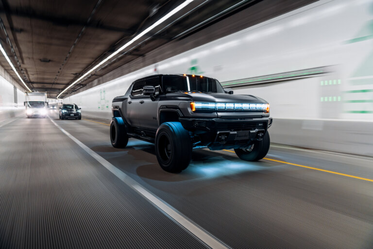 Black Hummer EV truck driving through a tunnel with glowing blue underglow lights.