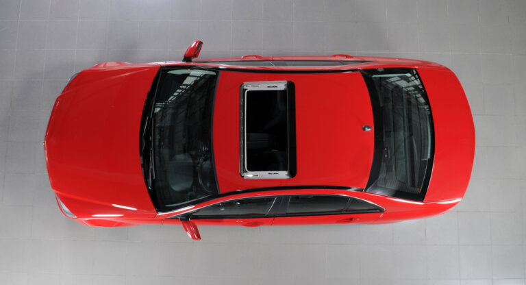 An overhead view of a red car with an open sunroof, parked on a light-colored tiled floor.
