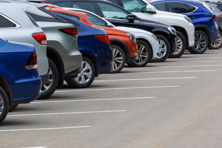 row of different color cars on asphalt parking lot at cloudy summer day